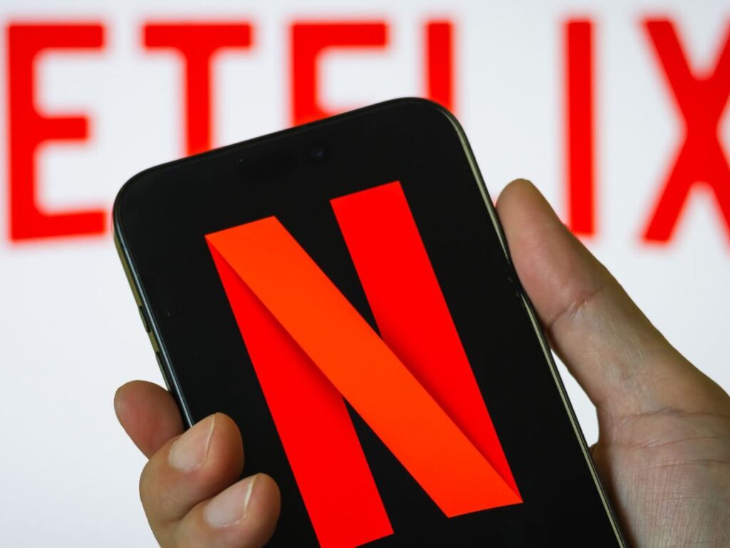 logo de netflix de fondo con persona sosteniendo un telefono celular